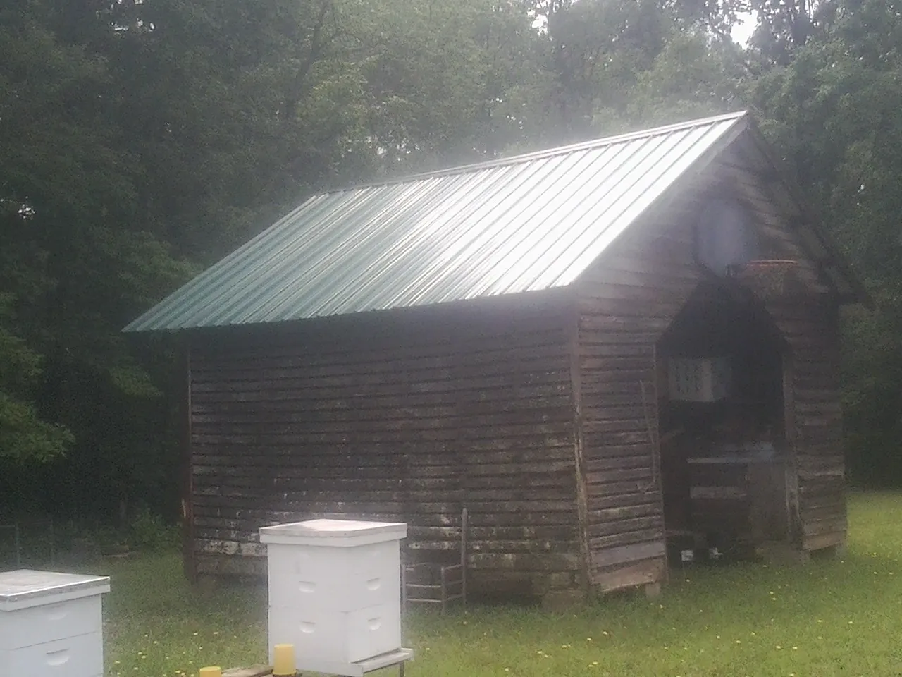 Green metal roof on a weathered barn beside stacked beehives in Commack