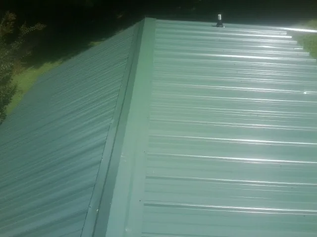 New green metal panels meeting at the ridge of a roof — Flat Roof Repair work by our crew in Commack