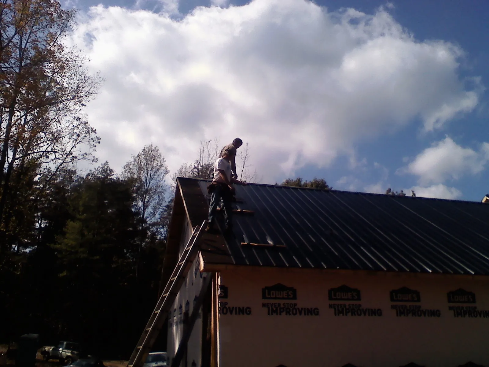 Roofer fastening dark metal panels high against a cloudy sky, from a Roof Inspection job in Commack