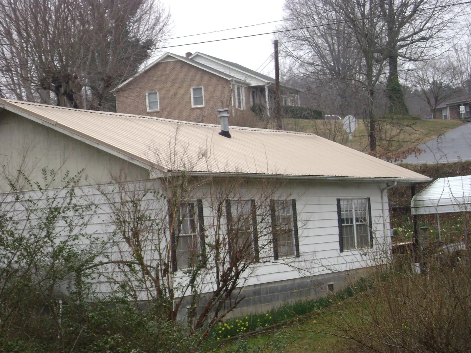 Tan metal roof on a white sided house set into a hillside — Commercial Roofing by Roofing Brothers in Commack