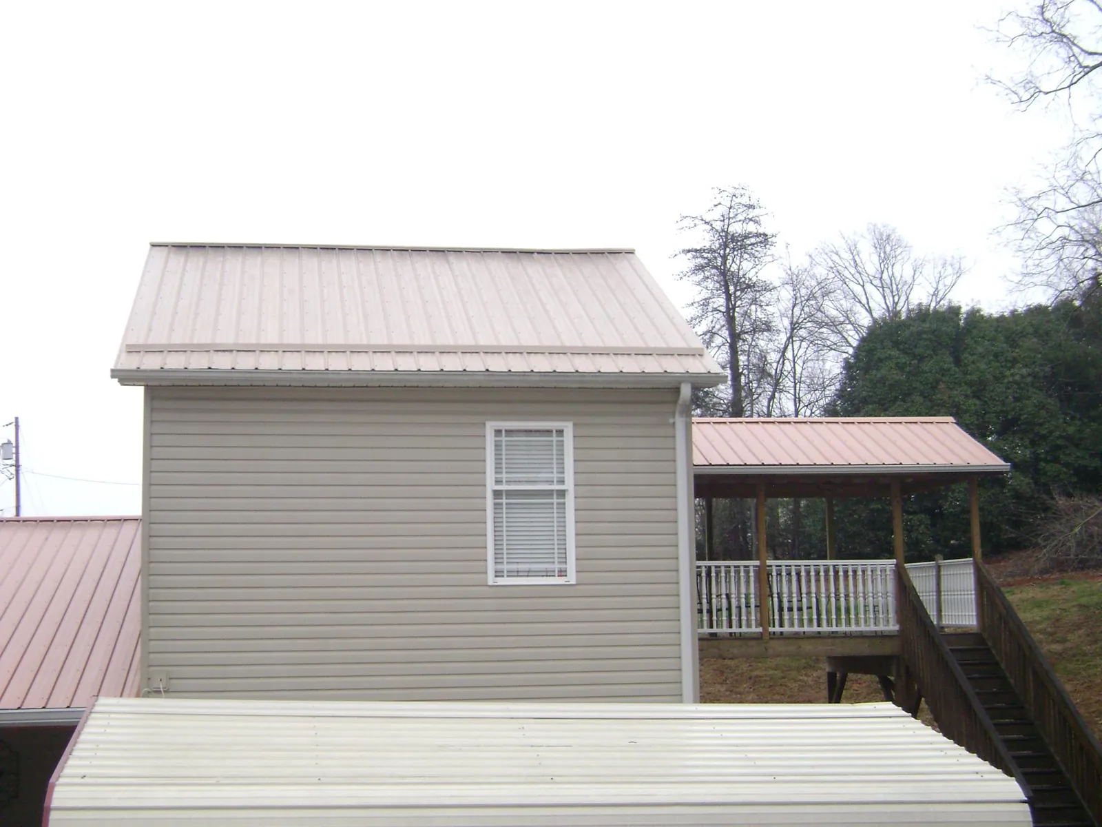 Tan metal roofs on a two story addition and attached porch, from a Roof Replacement job in Commack