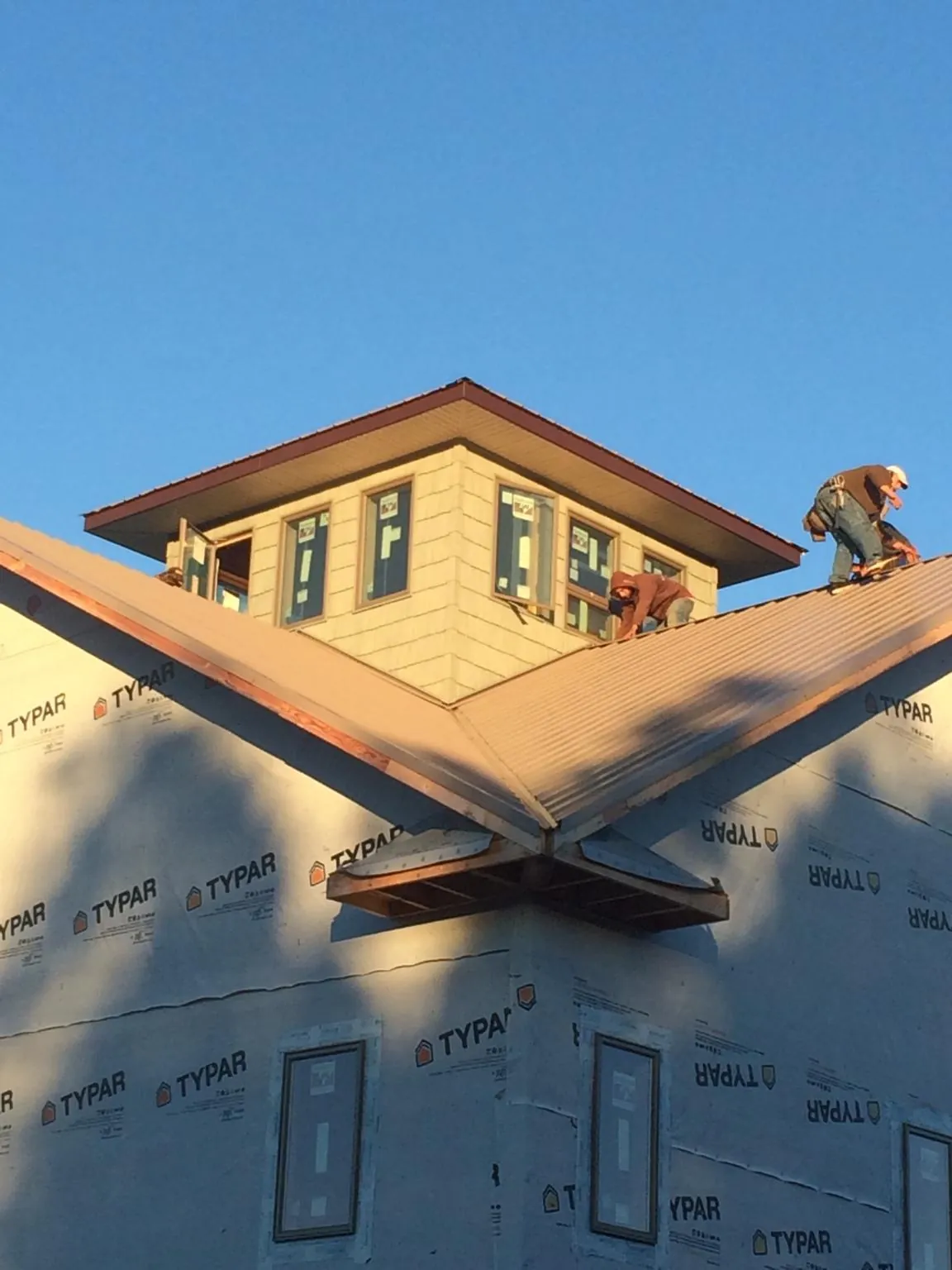Roofers working around a rooftop cupola on a new metal roof at sunset — Roof Waterproofing in Commack by Roofing Brothers